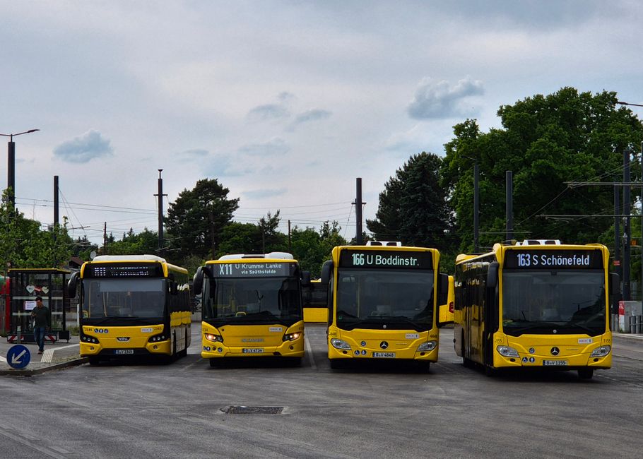 Four yellow buses parked in a line at a Berlin bus station on a cloudy day.